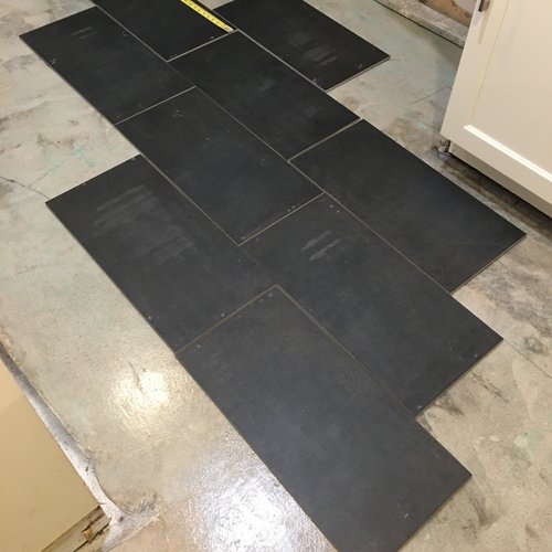 Dark floor tile layout in progress beside an exposed lower wall